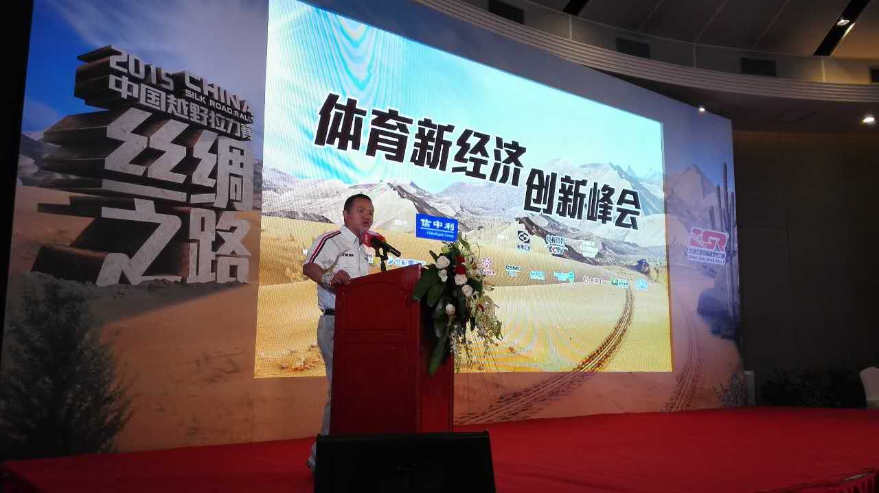 James TJ Lee speaking at a lectern before a large rally-themed conference screen.